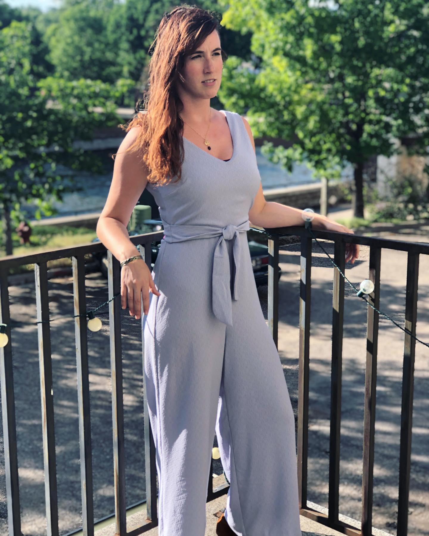 A woman in a gray jumpsuit is standing on a balcony.