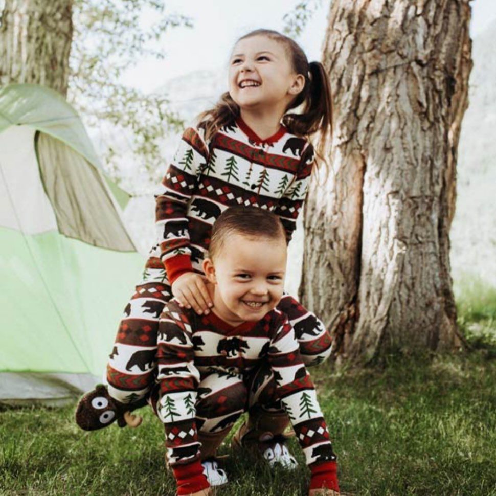A boy is carrying a girl on his shoulders in front of a tent.