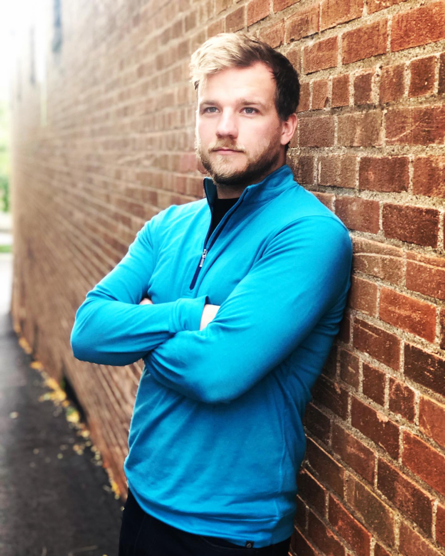 A man leaning against a brick wall with his arms crossed