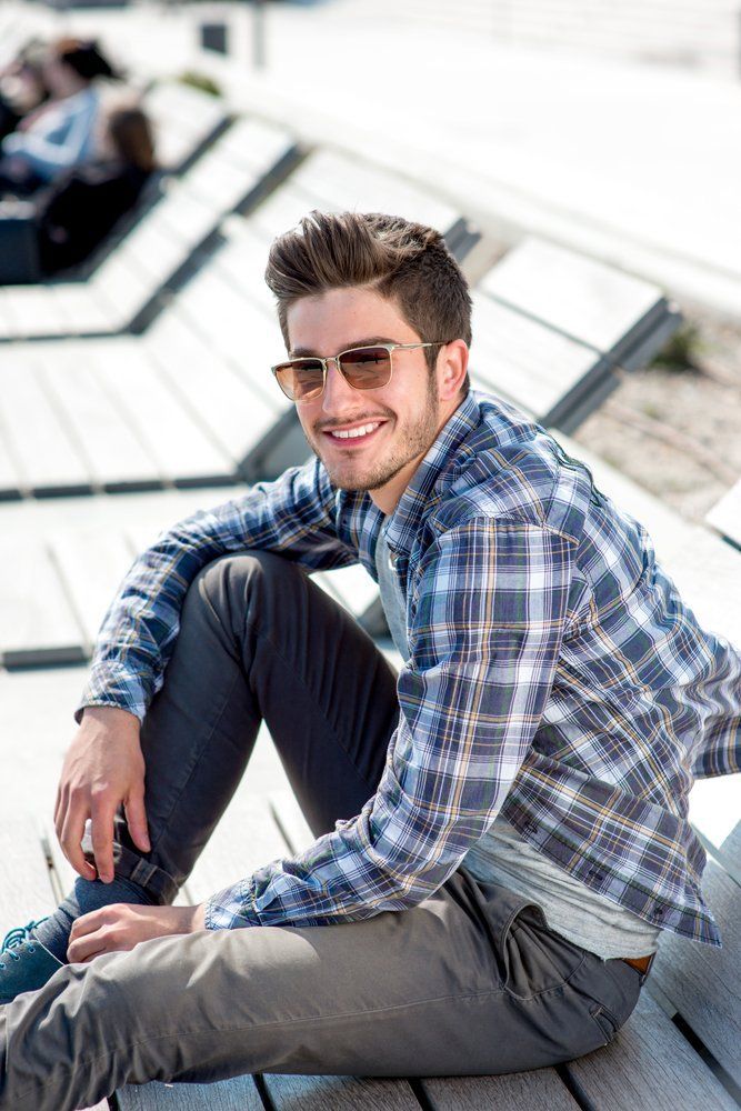 A young man wearing sunglasses is sitting on a wooden bench.