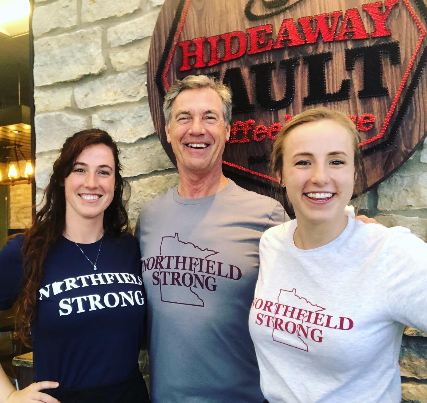 Three people are posing for a picture in front of a sign that says hideaway ault