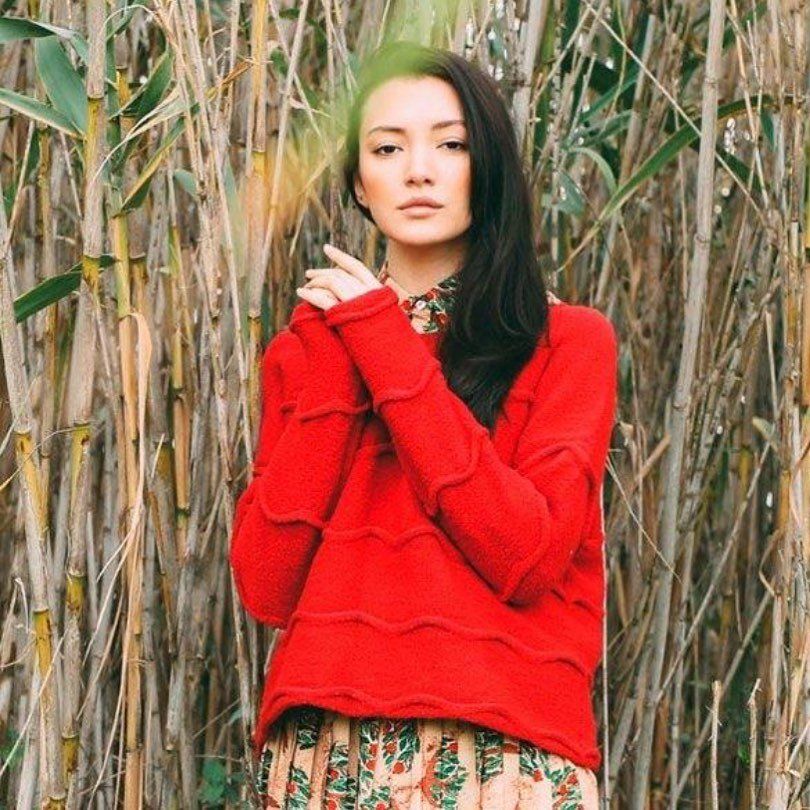 A woman in a red sweater is standing in a field of tall grass
