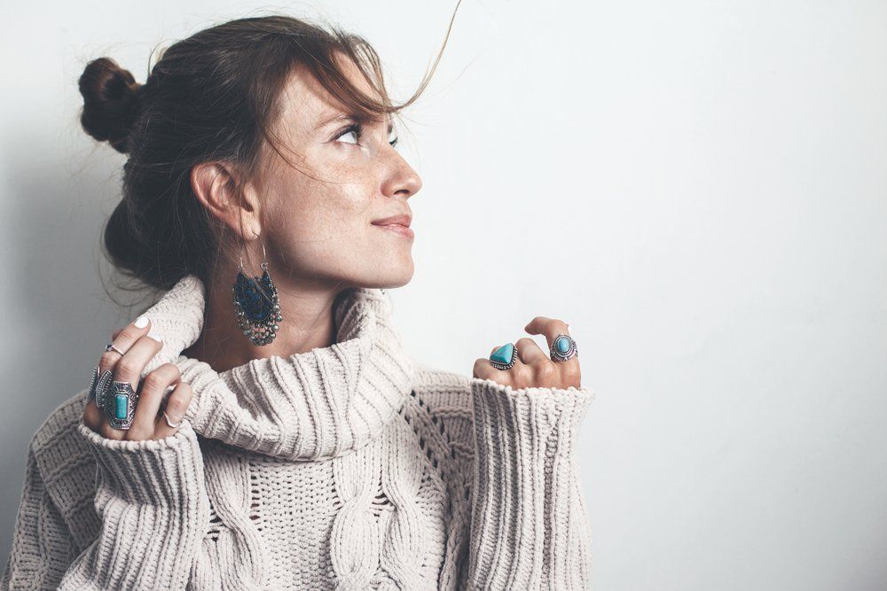 A woman wearing a sweater and earrings is looking up.