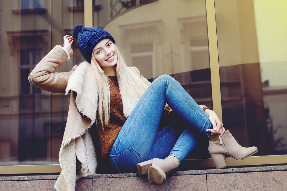 A woman is sitting on a window sill wearing a hat and jeans.