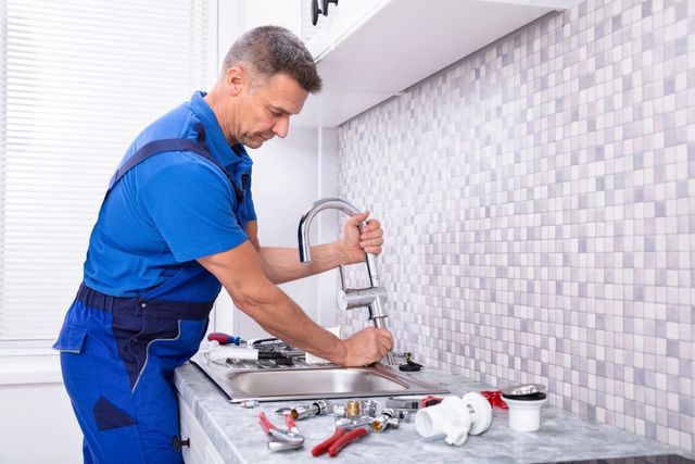 Plumber in blue uniform fixing a kitchen sink with tools on the counter