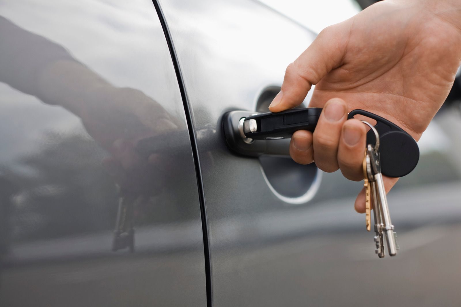 A hand inserts a key into the door lock of a gray car.