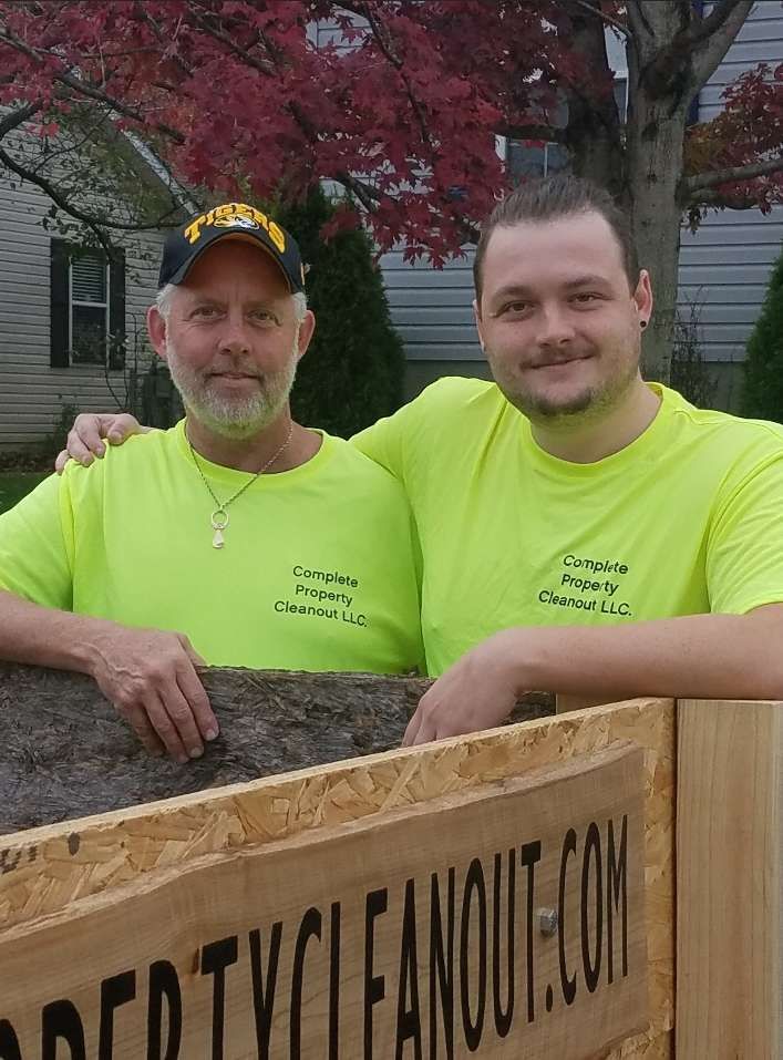 Two men are posing for a picture in front of a sign that says propertycleanout.com