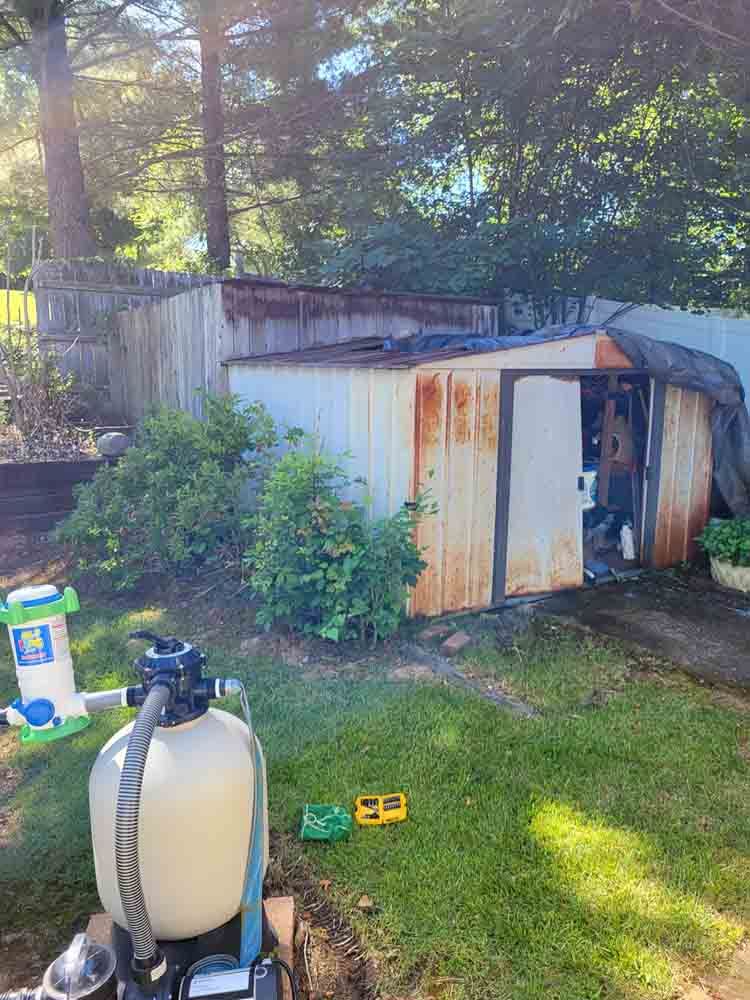 A pool filter is sitting in front of a shed in a backyard.