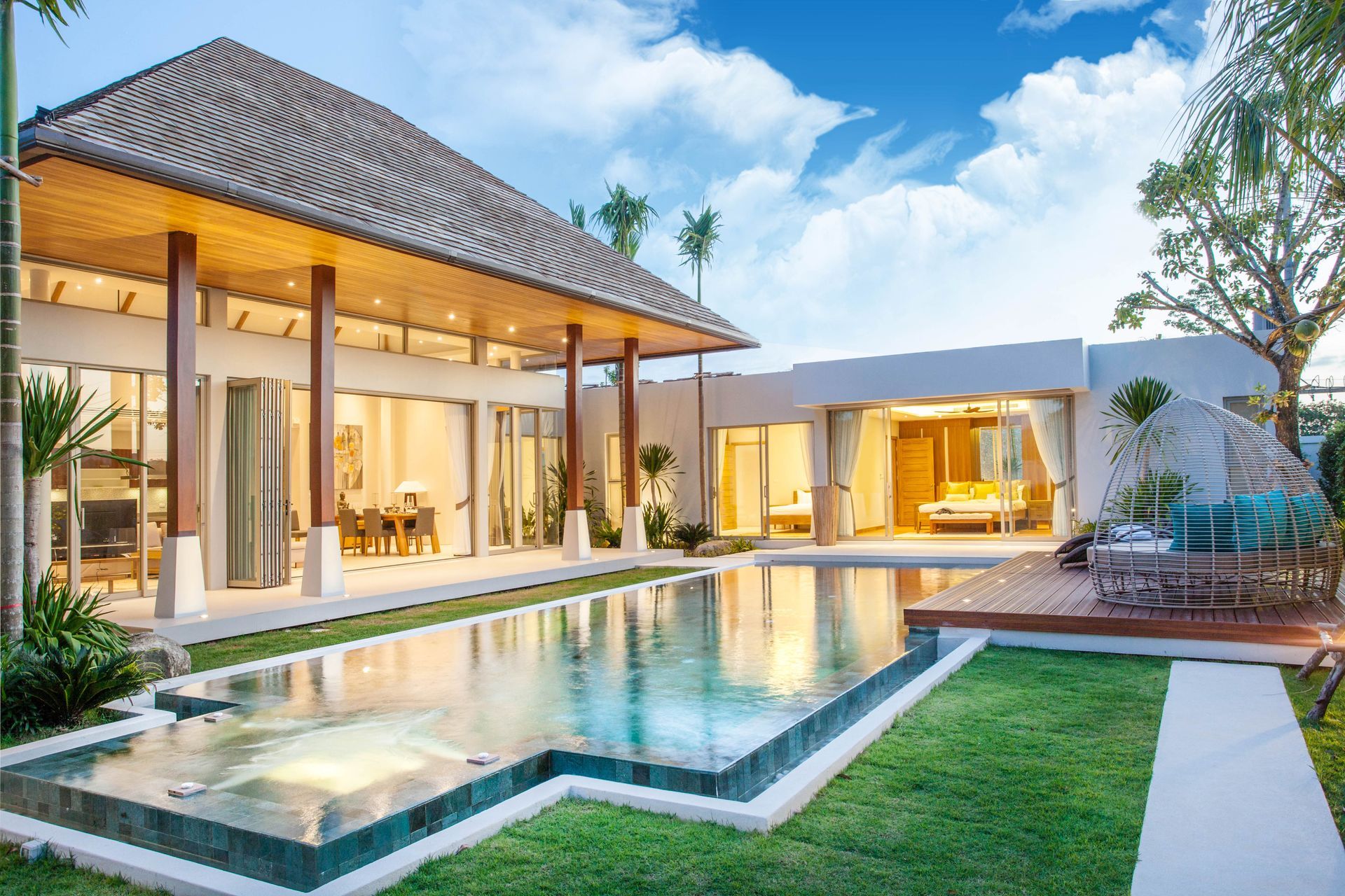 A luxury villa with a tiled roof, open living area, and swimming pool set in a tropical, sunlit landscape.