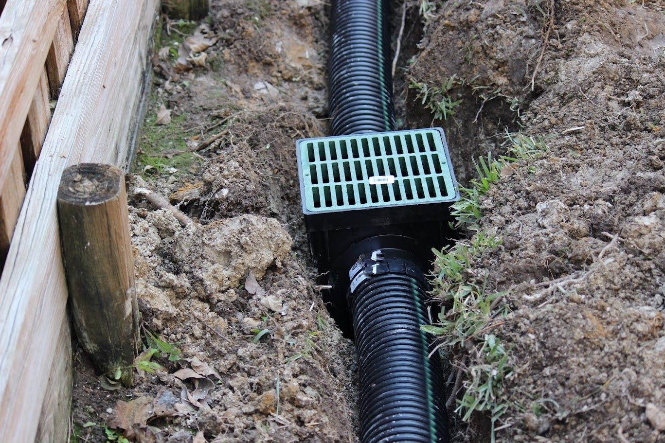 A black pipe is laying in the dirt next to a wooden fence installed by Elite Outdoor Living Solutions in Edgemere Park, OKC.