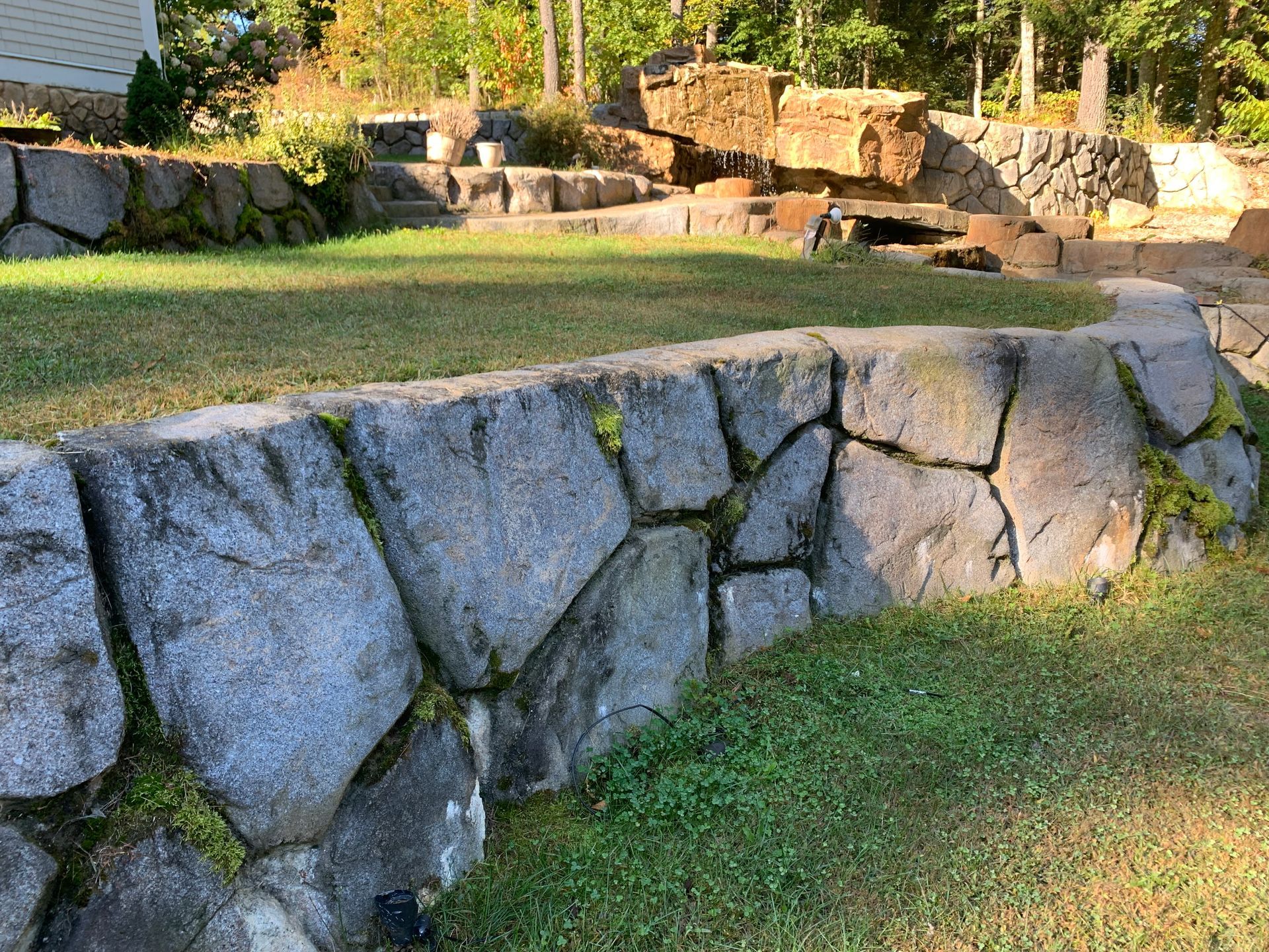 Elite Outdoor Living Solutions installed a large stone retaining wall surrounding lush greenery in Quail Creek, OKC.