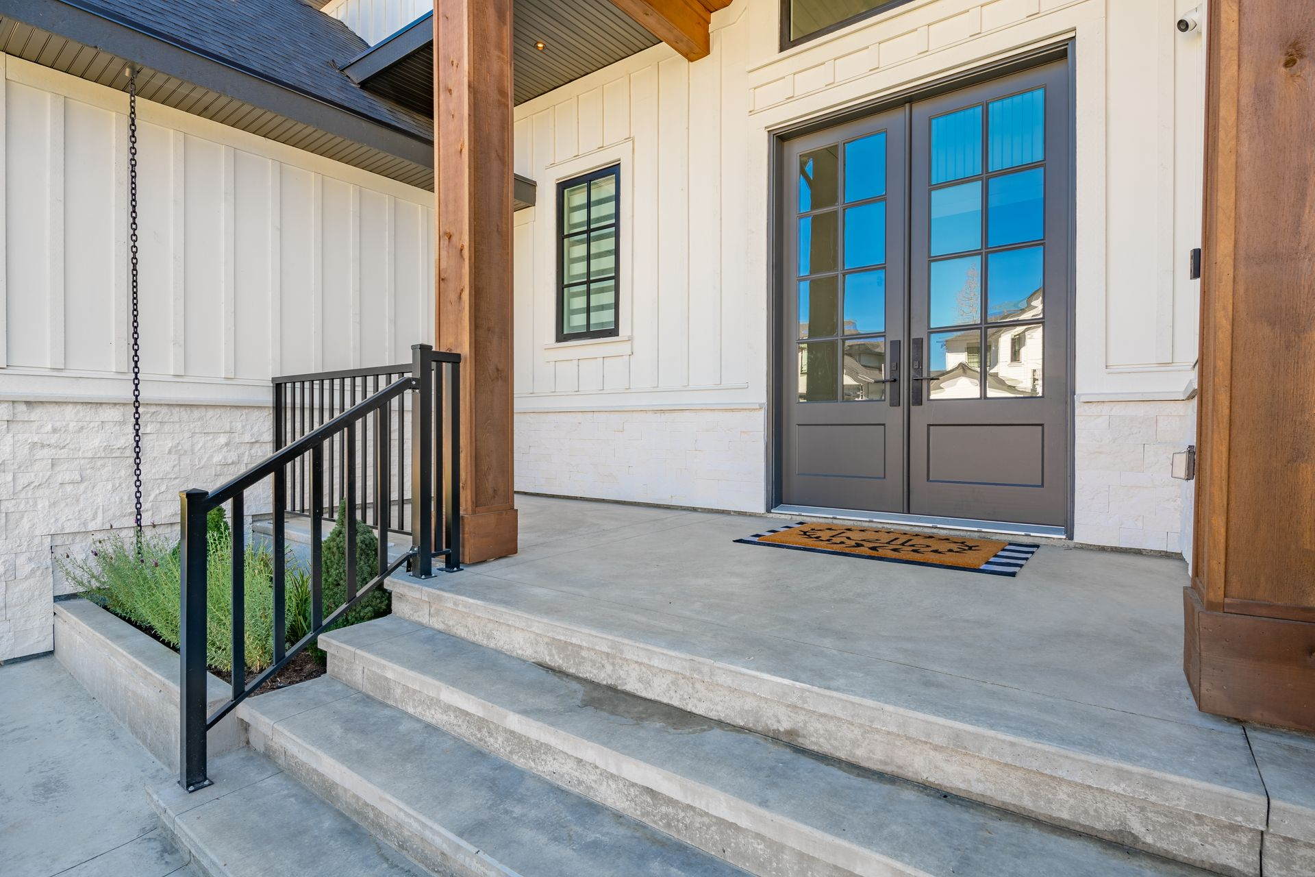 Modern home entryway with smooth concrete steps, black metal railing, and double glass doors.