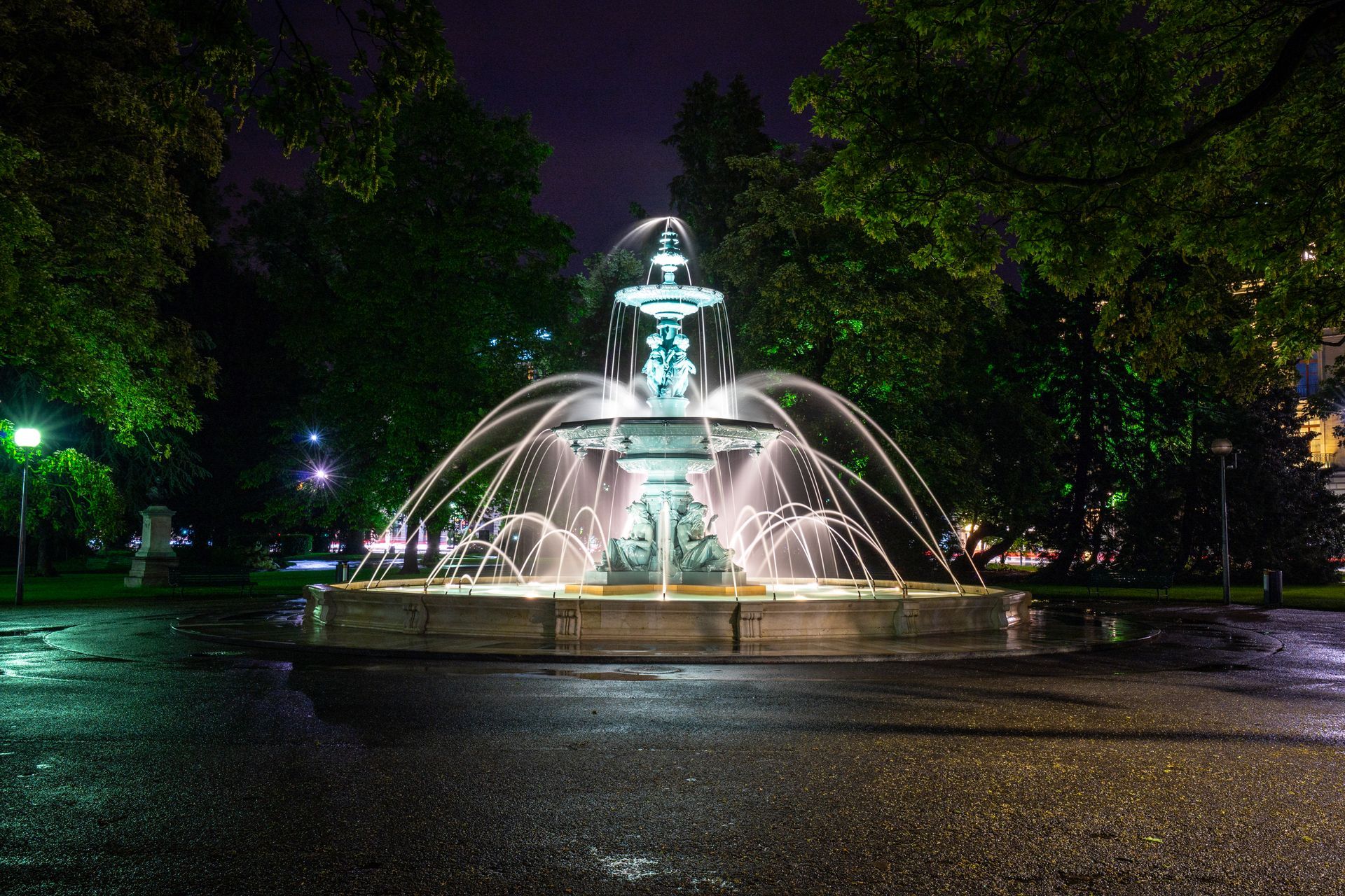 A fountain is lit up at night in a park.