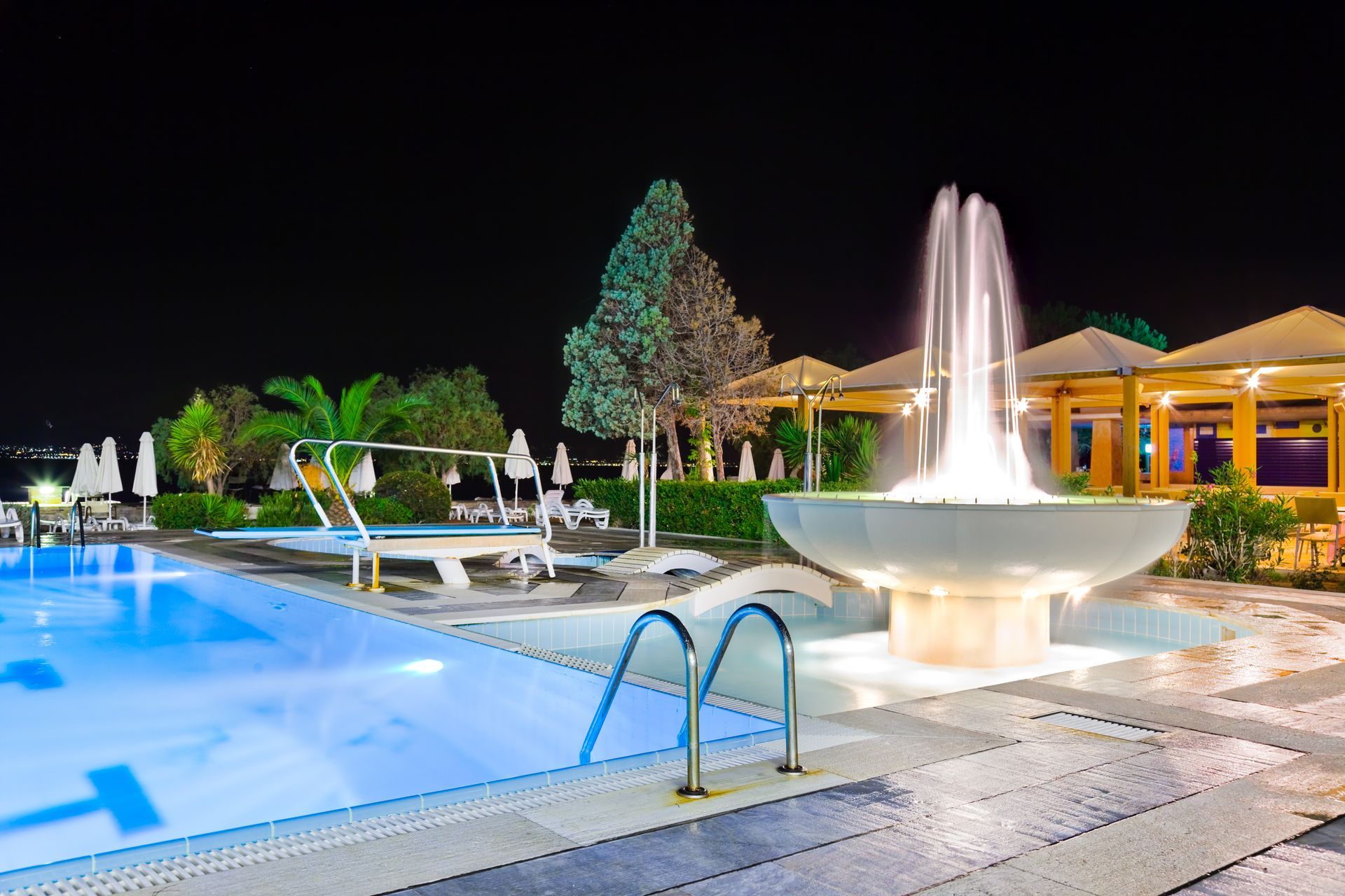 A large swimming pool with a fountain in the middle of it at night.