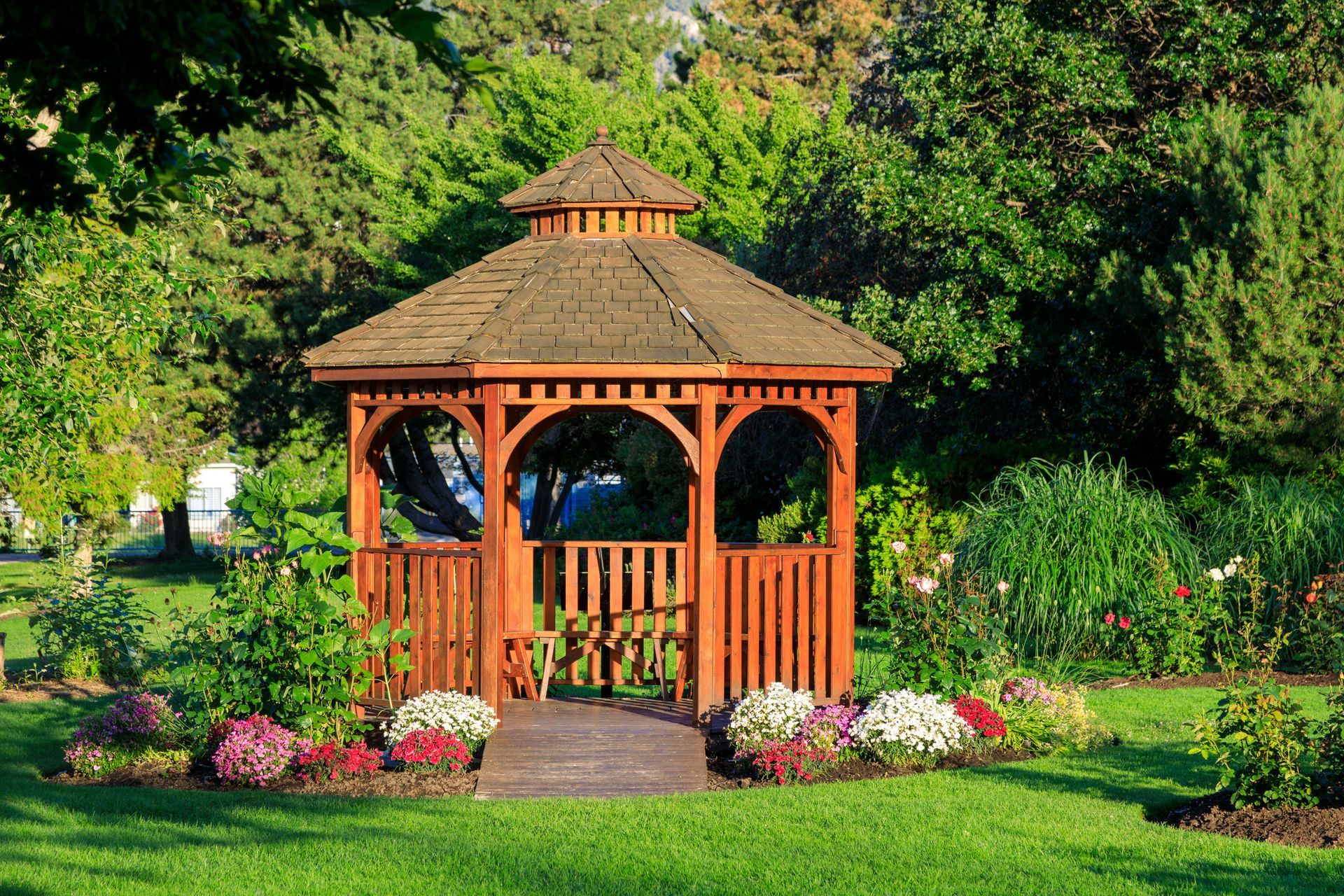 A wooden gazebo in a park surrounded by trees and flowers