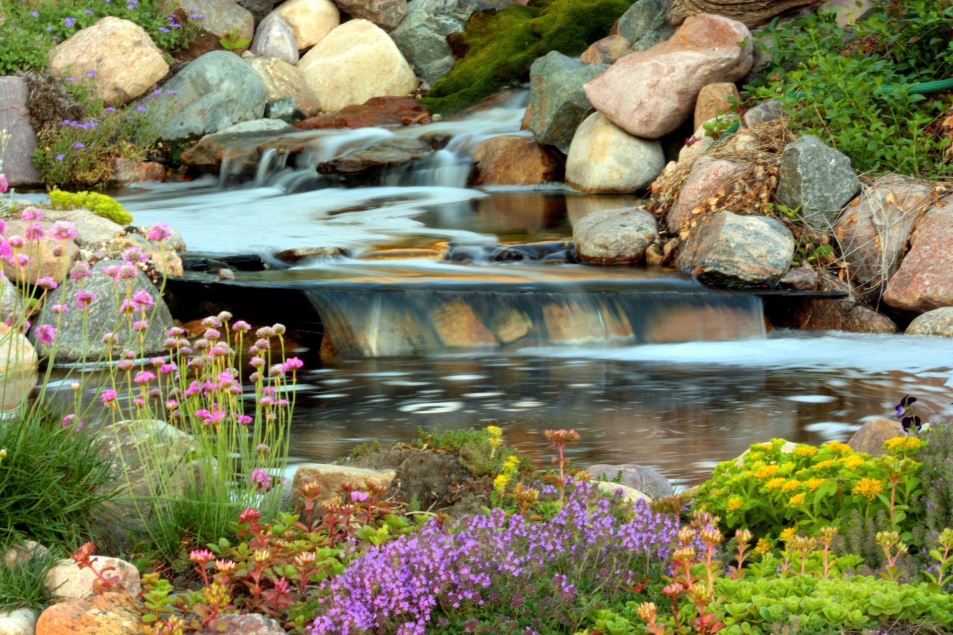 A waterfall is surrounded by rocks and flowers in a garden.