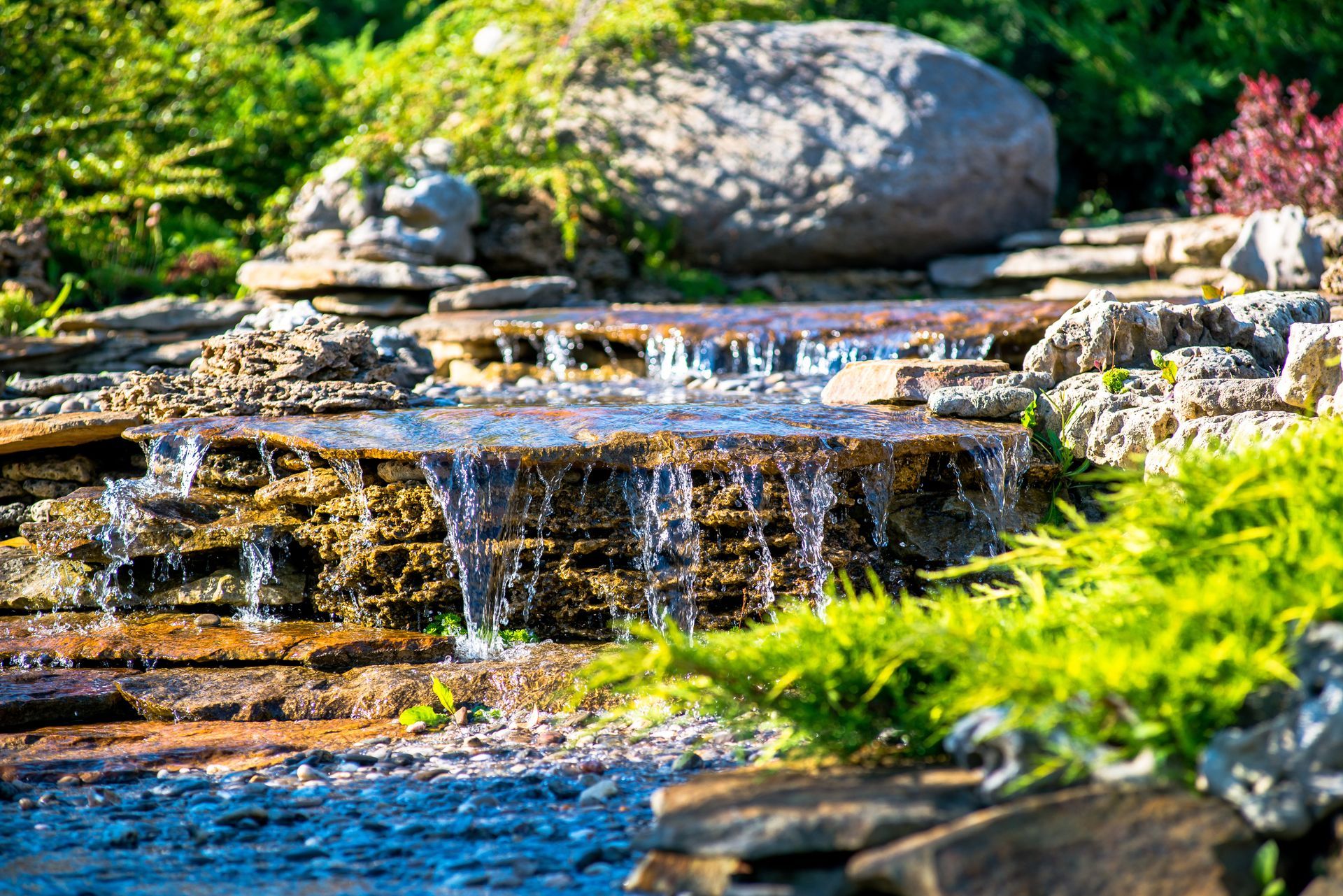 A waterfall is surrounded by rocks and plants in a garden.