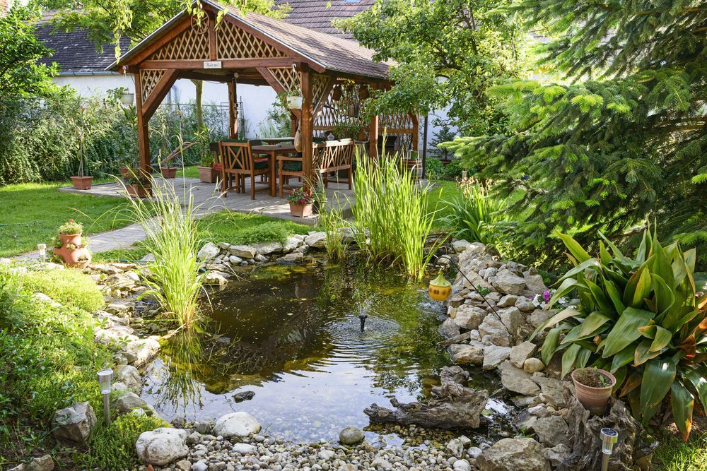 A pond in a garden with a gazebo in the background.
