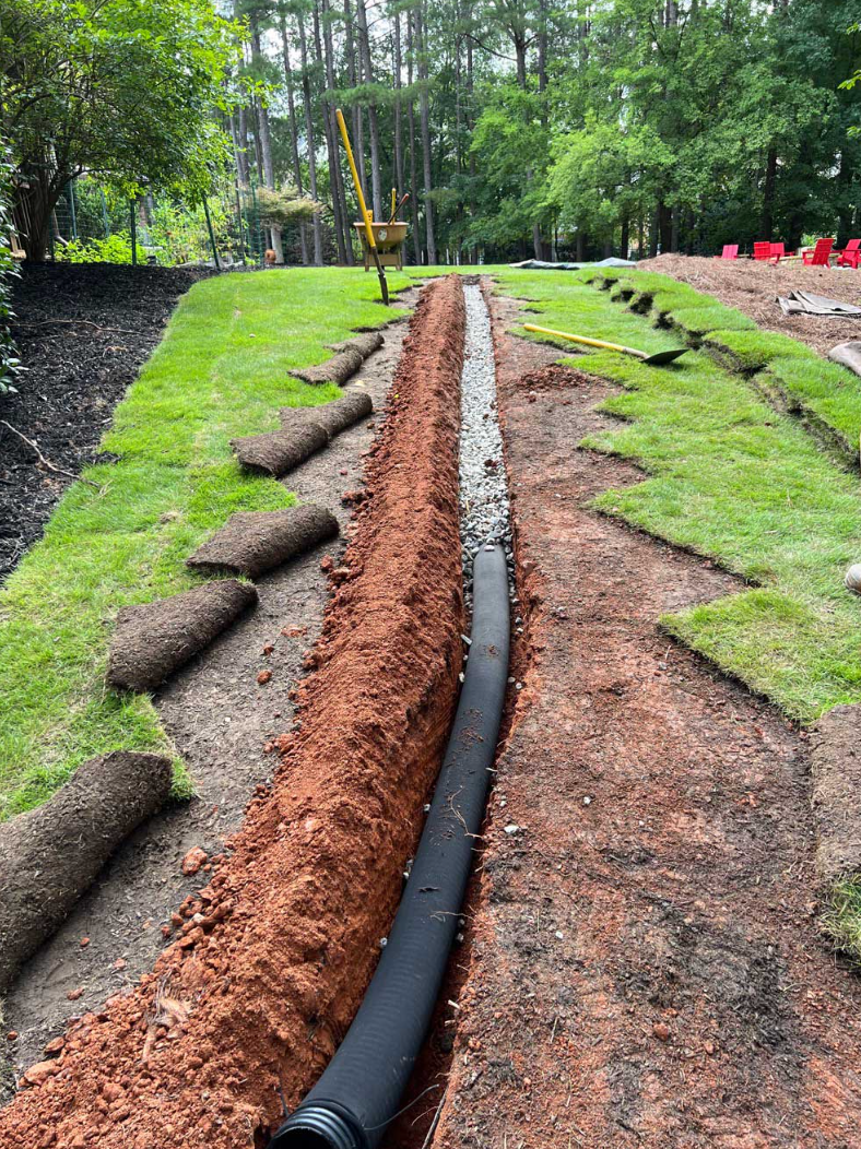 Elite Outdoor Living Solutions installing French drains with dirt on it in a lush backyard in Choctaw, OK.