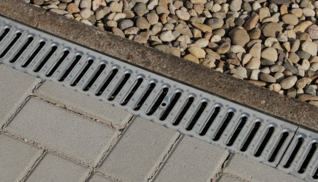 Elite Outdoor Living Solutions is installing a metal channel drain on a sidewalk next to gravel in Belle Isle, OKC.