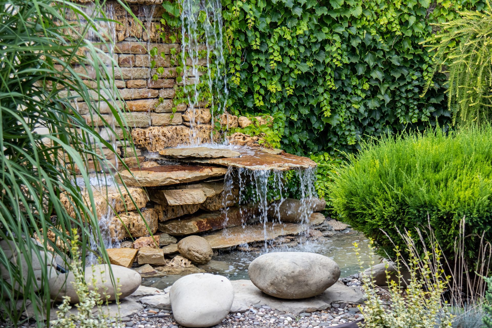 A small waterfall is surrounded by rocks in a garden.