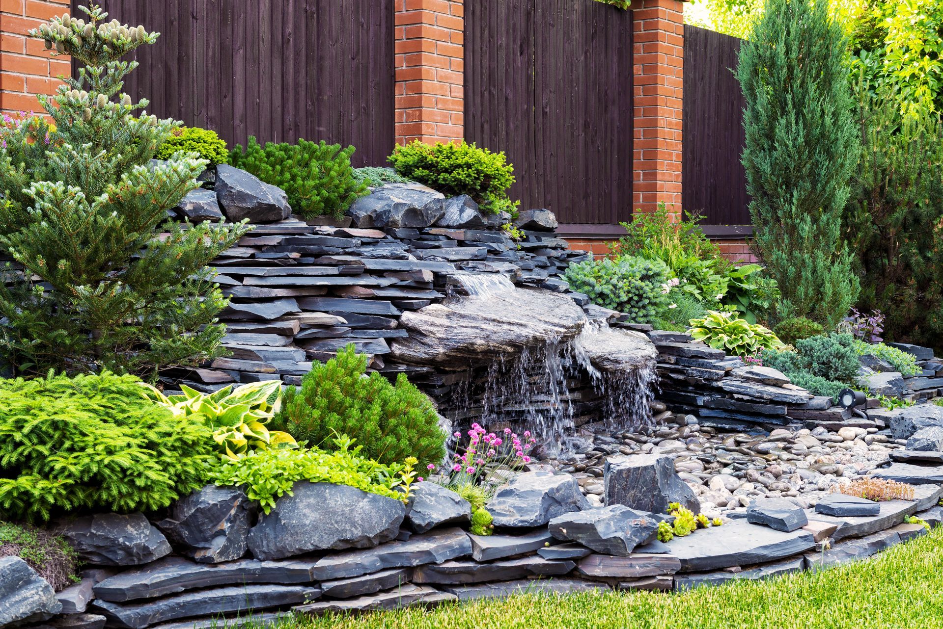 A waterfall is surrounded by rocks and plants in a garden.