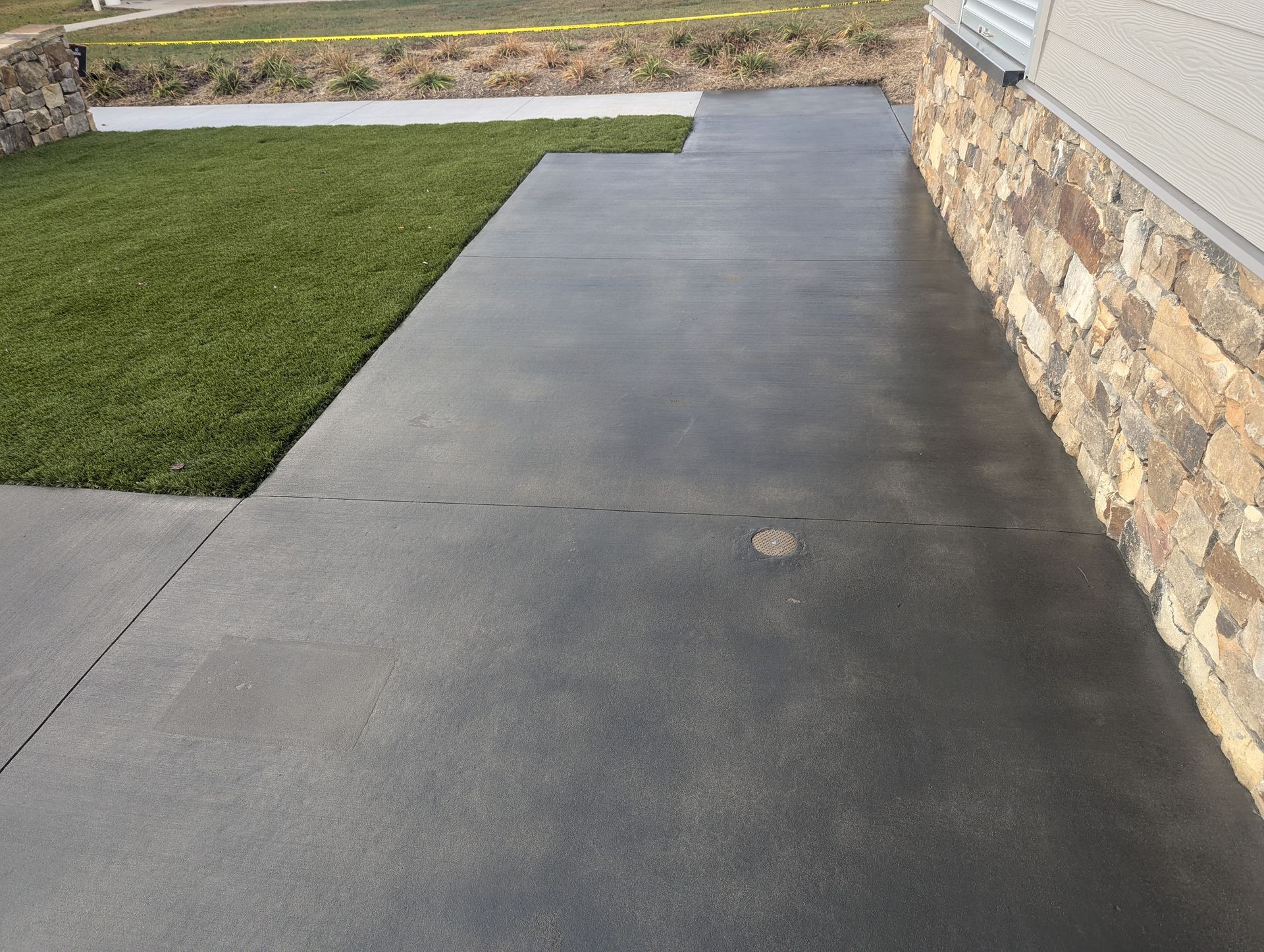 Elite Outdoor Living Solutions installed stained concrete near a stone wall and grass in Oklahoma City.