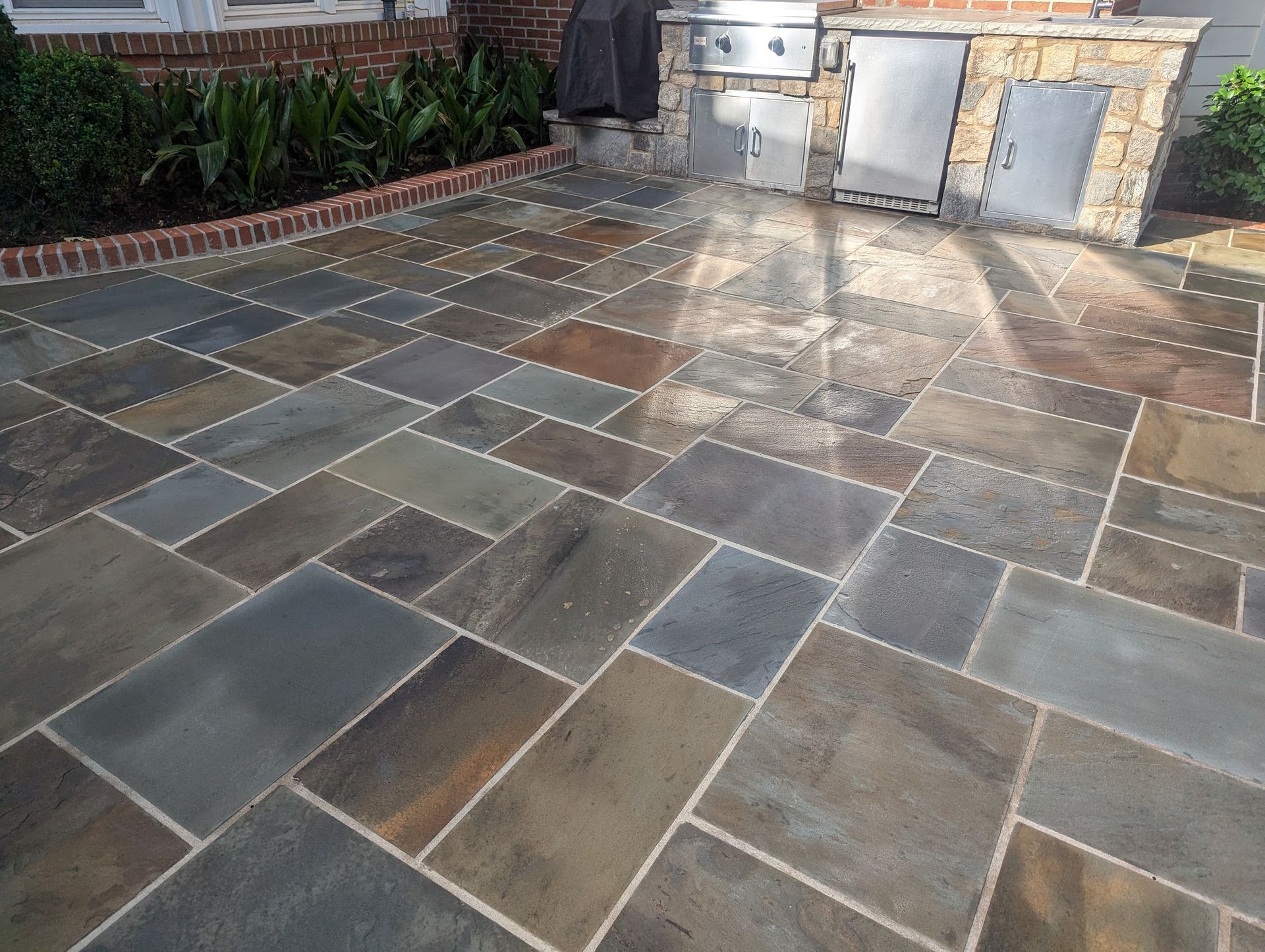 A stone patio with a grill in the background installed by Elite Outoodr Living Solutions in Nichols Hills, OKC.