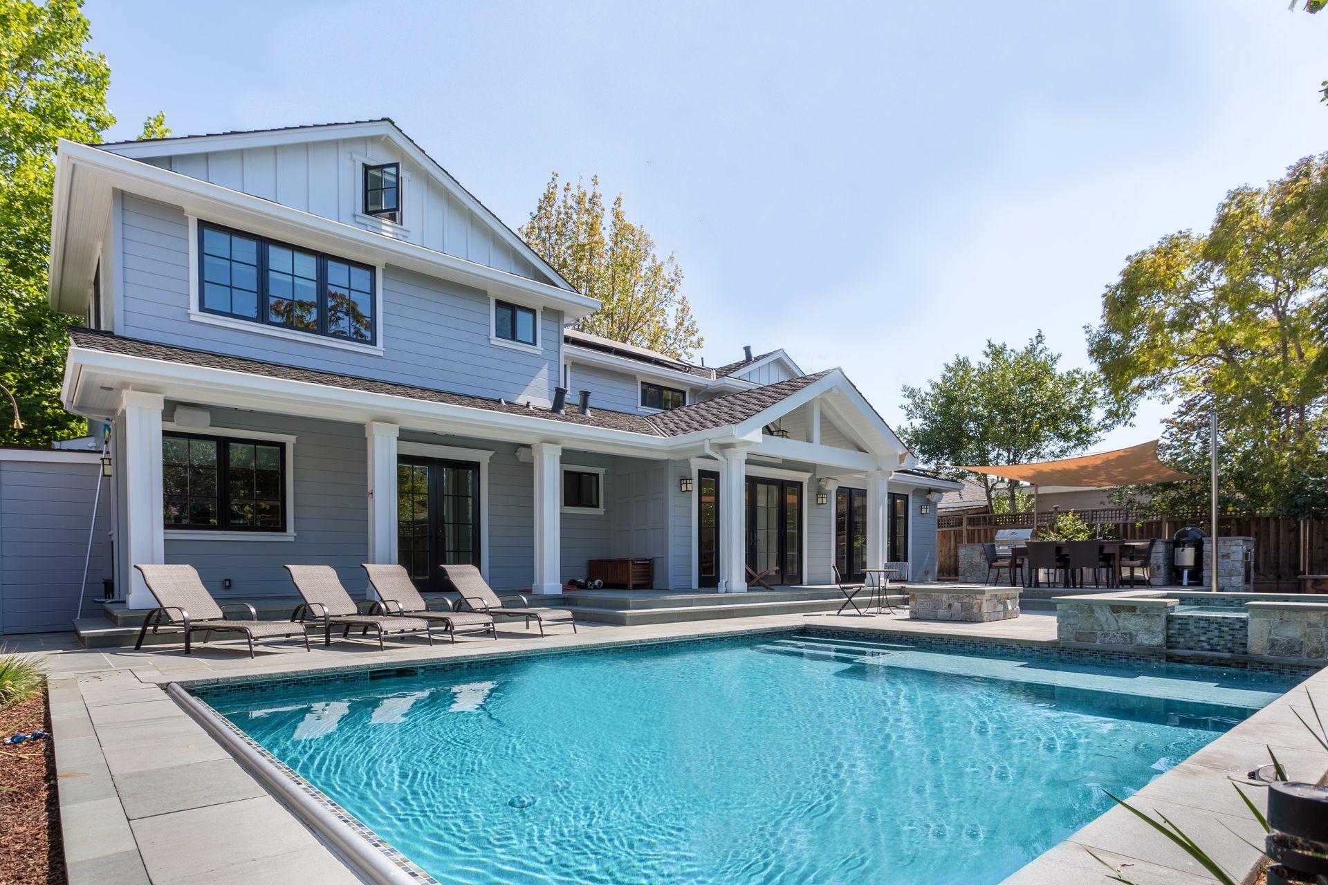 A two-story gray house with a pool in the backyard. Lounge chairs line the pool, sunny day.