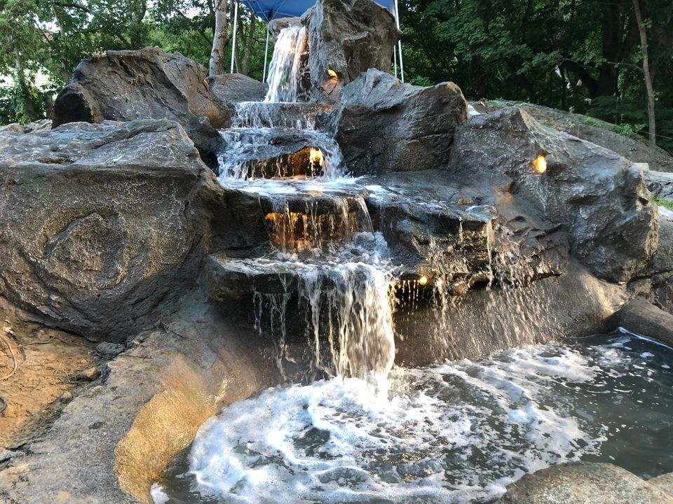 A waterfall is surrounded by rocks and plants in a garden.