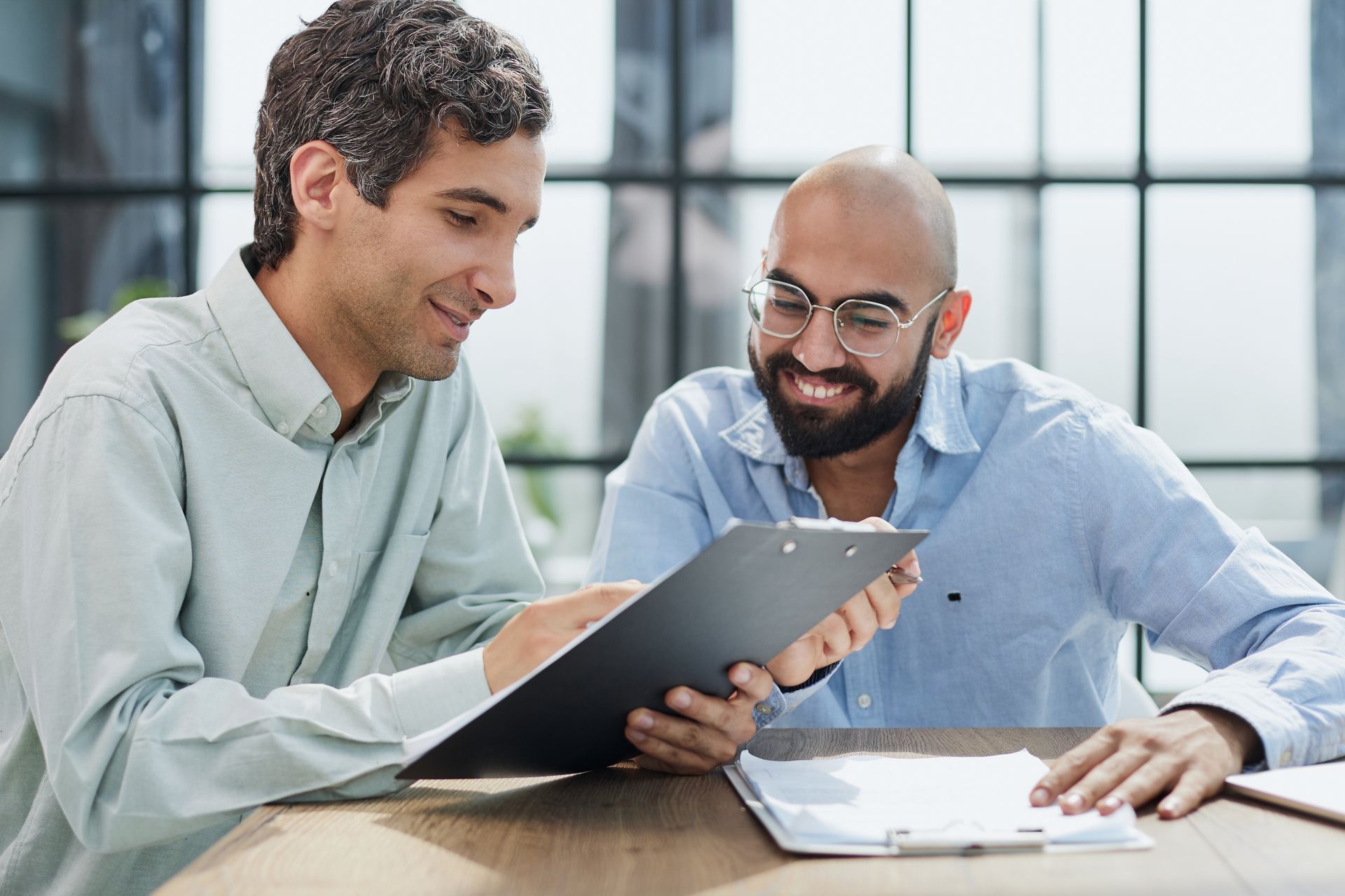 Two men are sitting at a table looking at a clipboard.