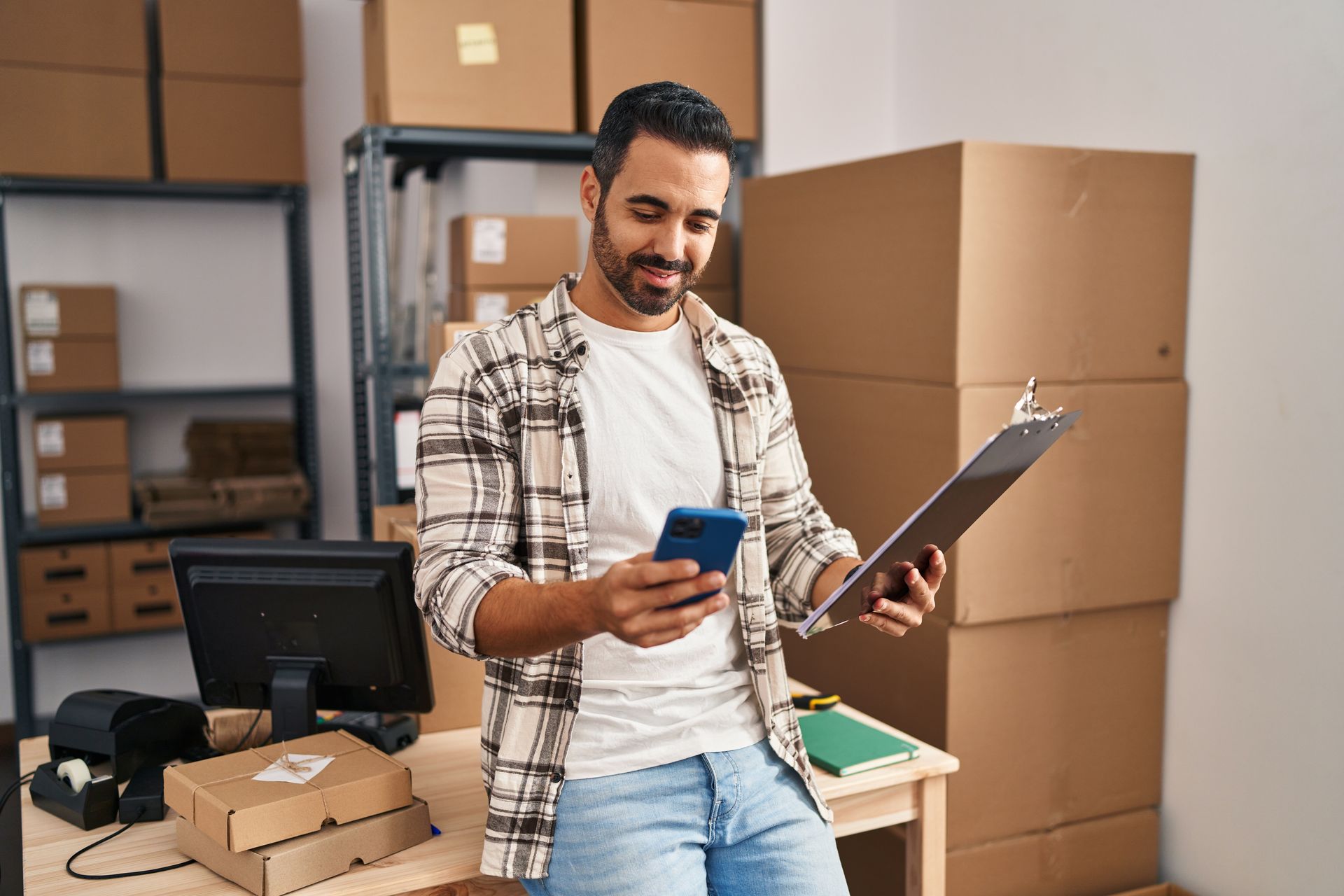 A man is holding a clipboard and a cell phone in a warehouse.