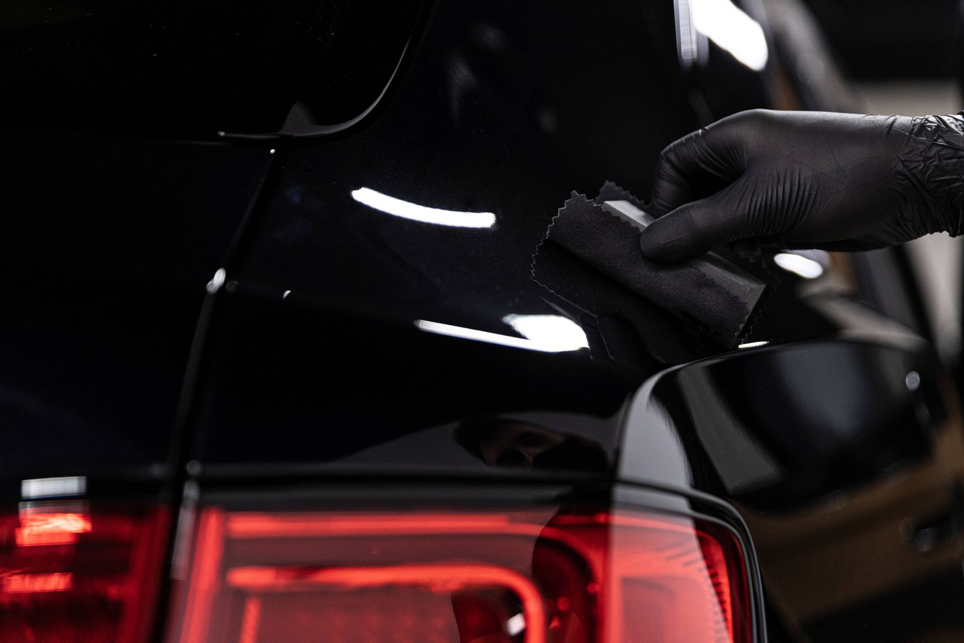 A person wearing black gloves is polishing the back of a black car.