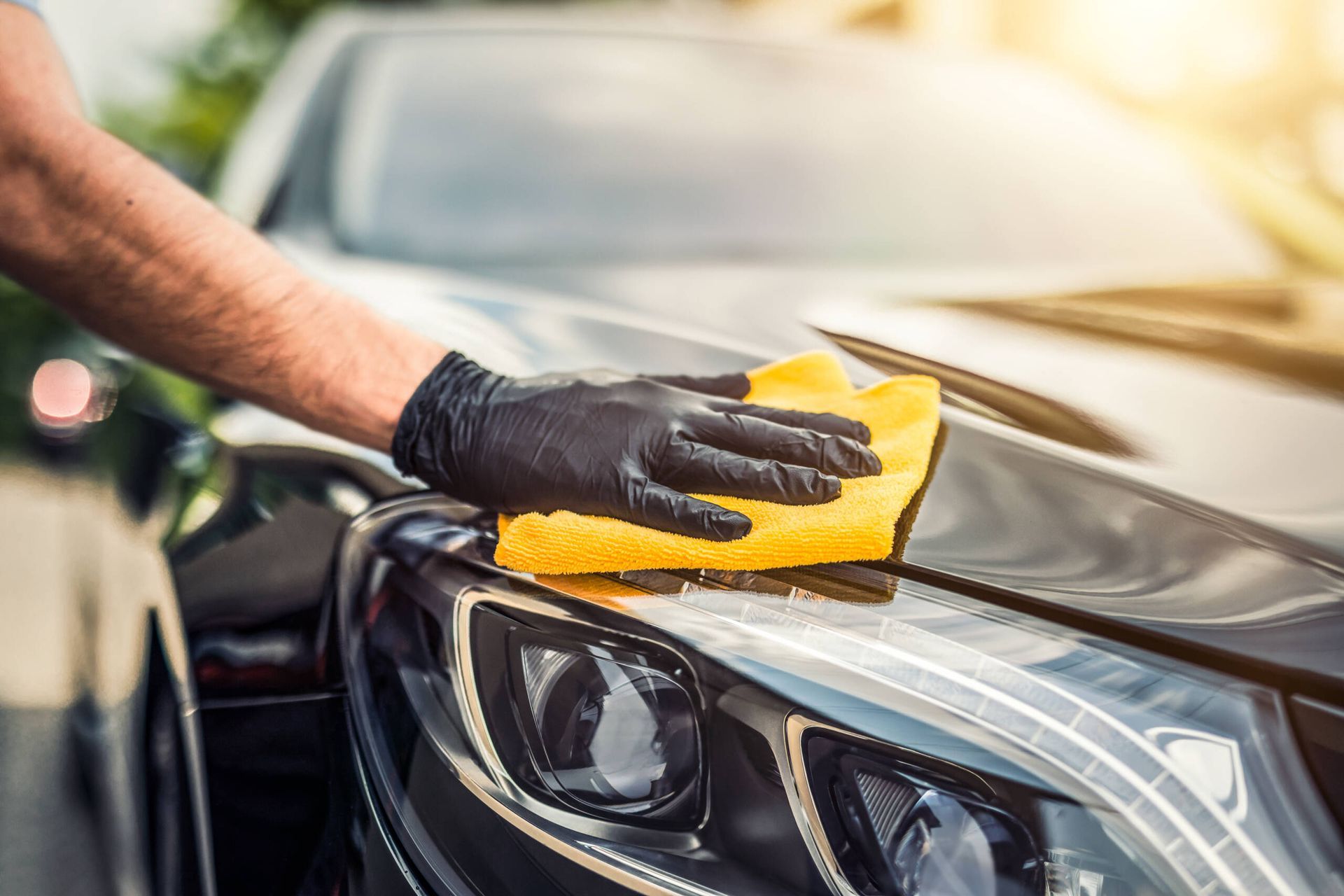 A man is cleaning a car with a yellow cloth.