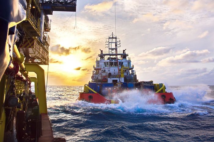 Large tug heading out to see with close up section of oil rig on left hand side