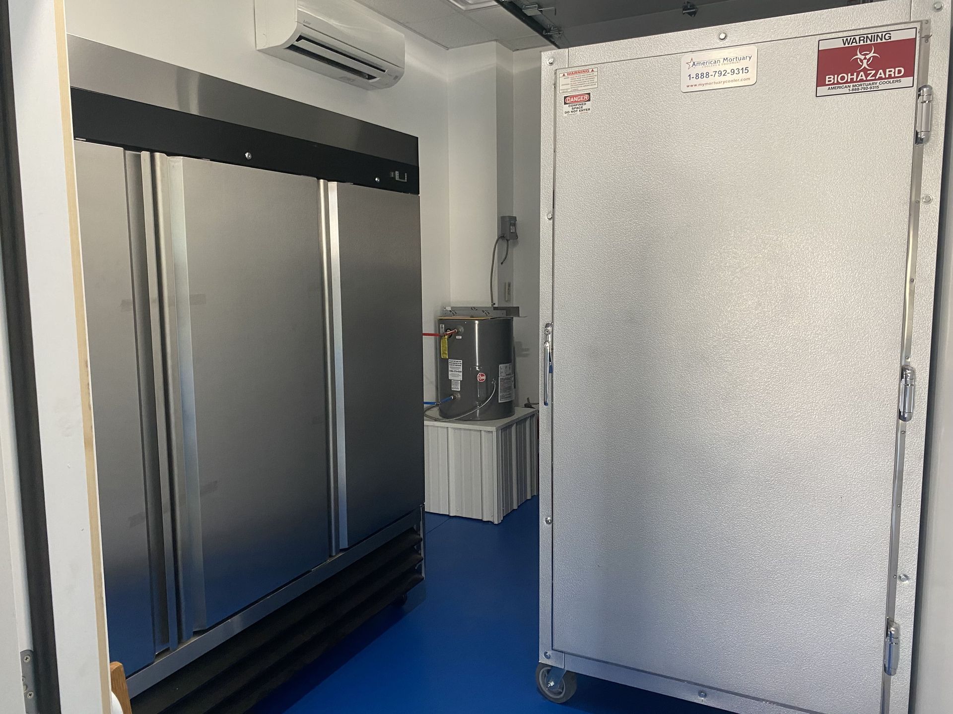 Open freezer doors reveal a small room with blue floor and equipment. Air conditioning unit on the wall.