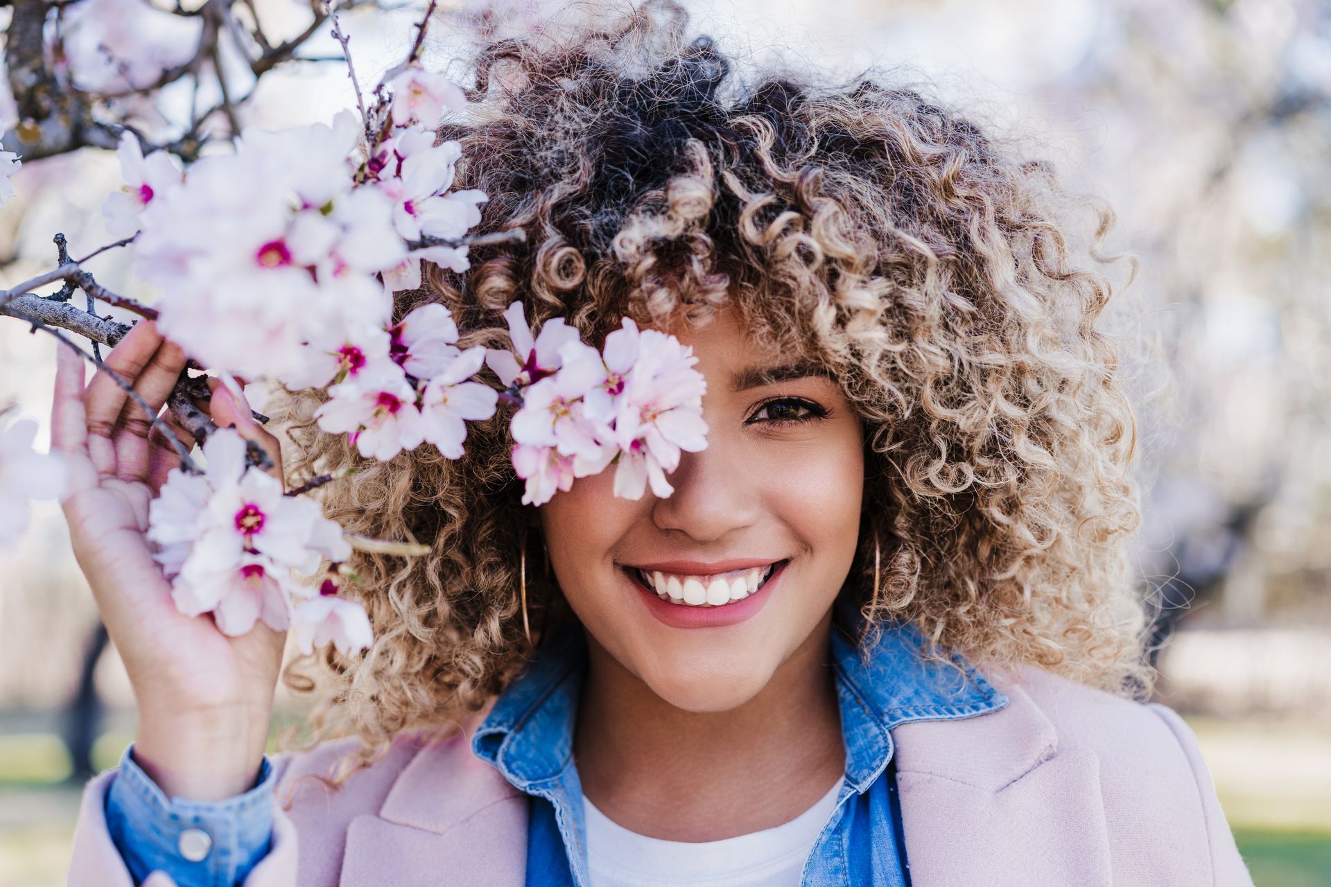 a woman with curly hair is holding a flower in front of her face .