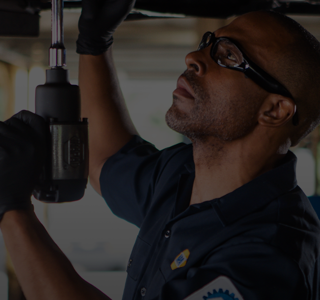 Mechanic wearing safety glasses, working on a vehicle, holding a tool, focused. | Northlake Automotive