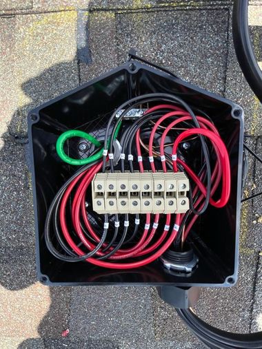 Open electrical junction box with bundled red and black wires and terminal blocks on pavement