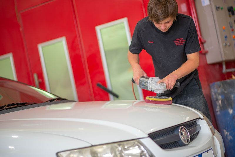 A man is polishing a white car in a garage.