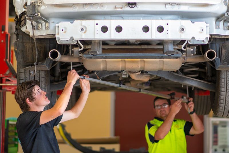 Two men are working on the underside of a car in a garage.