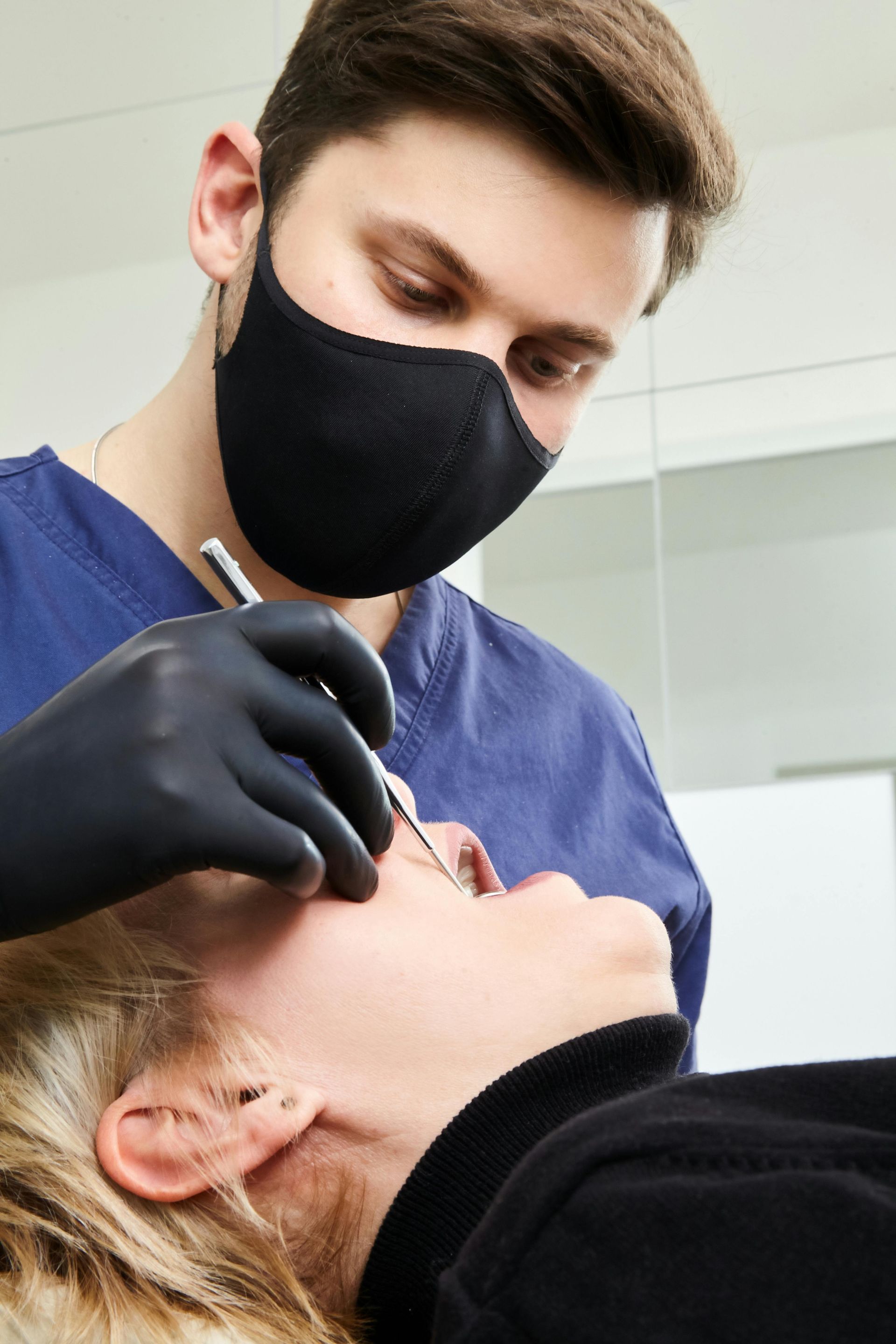 A dentist wearing a mask and black gloves is examining a patient 's teeth.