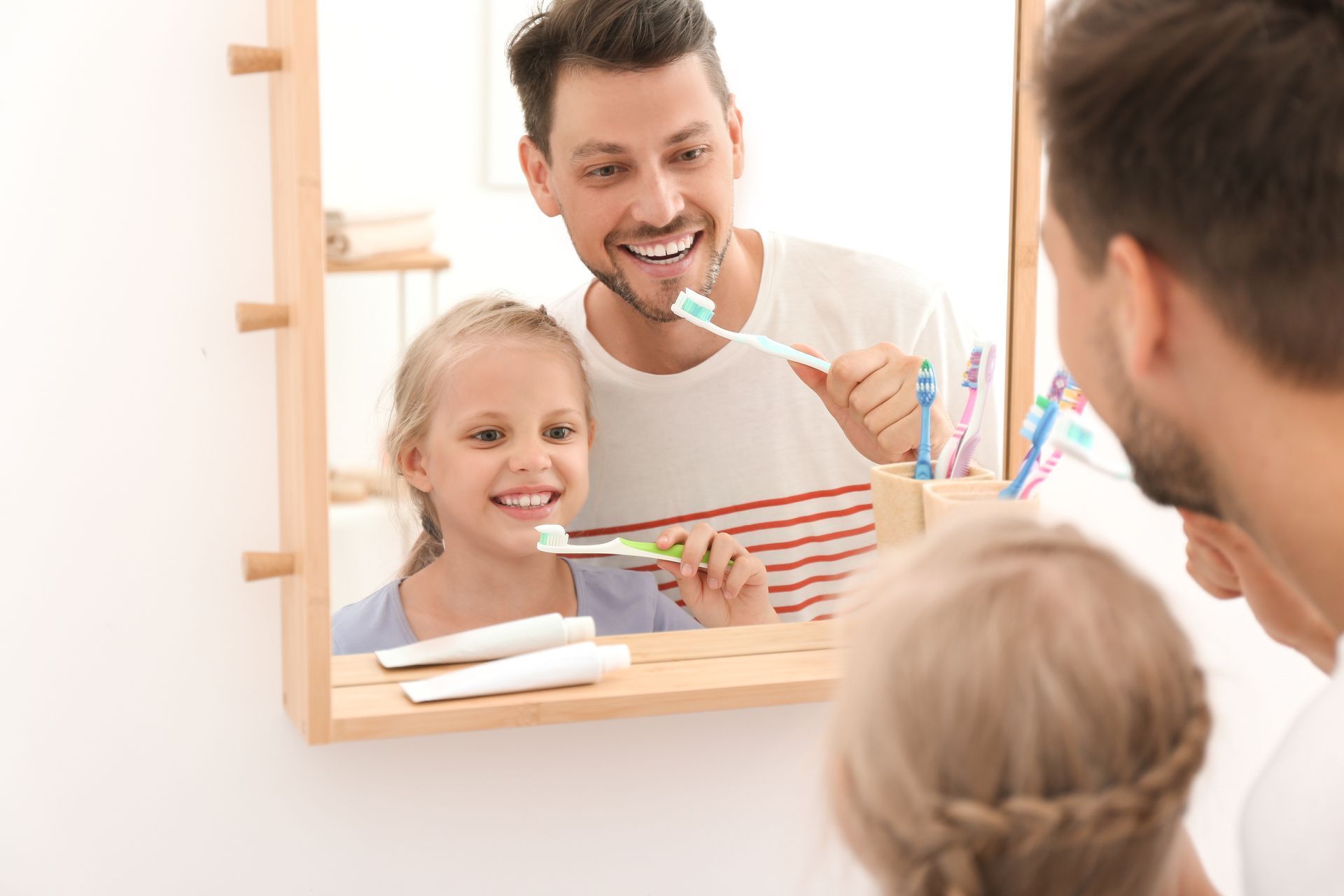 A man and a little girl are brushing their teeth in front of a mirror.