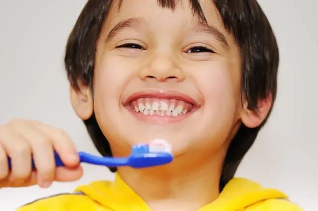 A young boy is brushing his teeth with a blue toothbrush