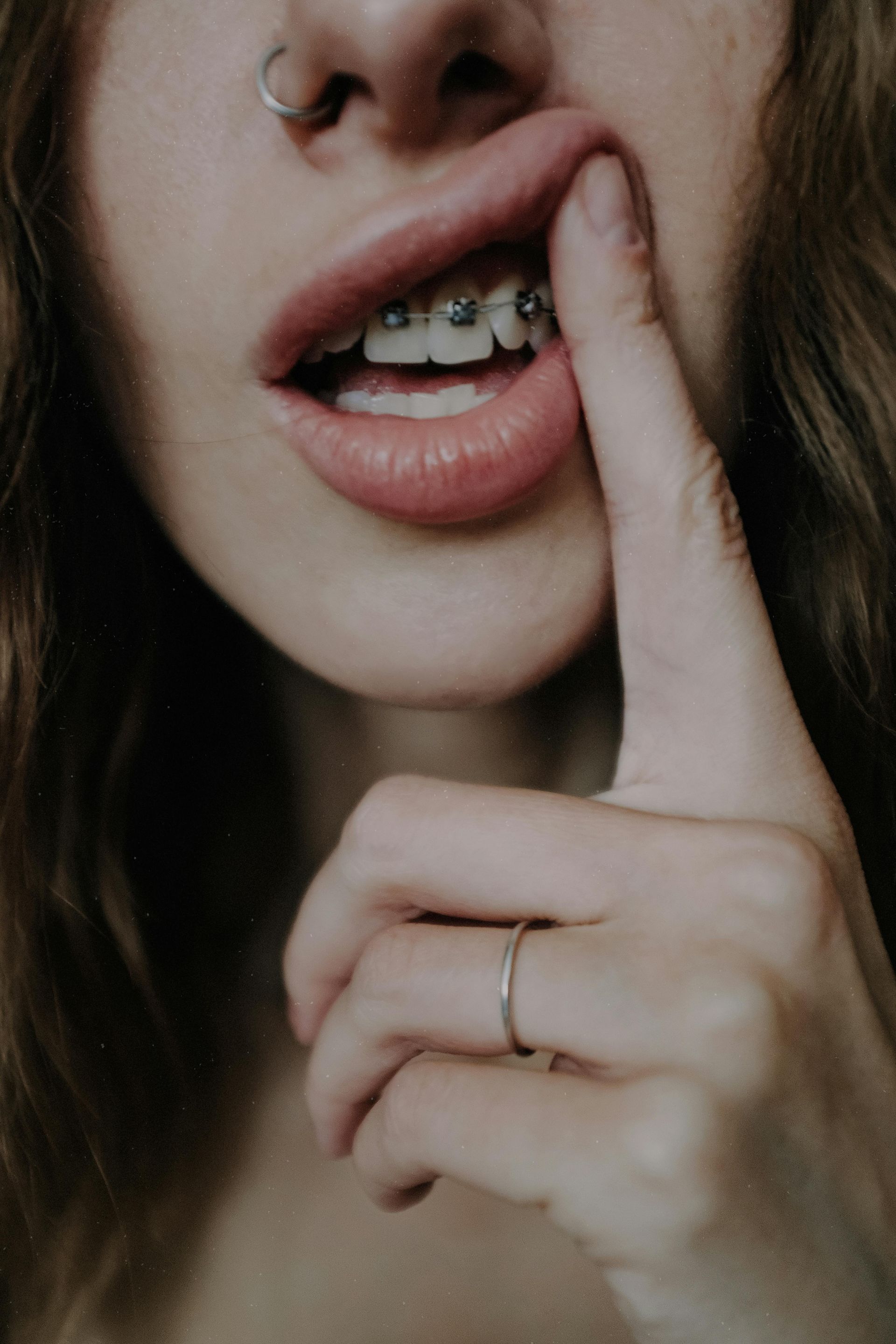 A woman with braces on her teeth is covering her mouth with her finger.