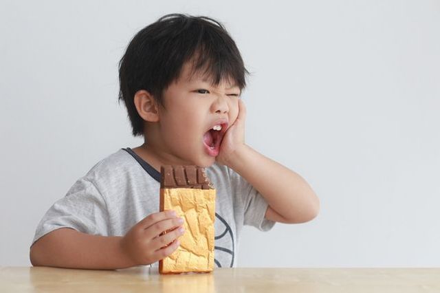 A young boy is sitting at a table eating a chocolate bar.