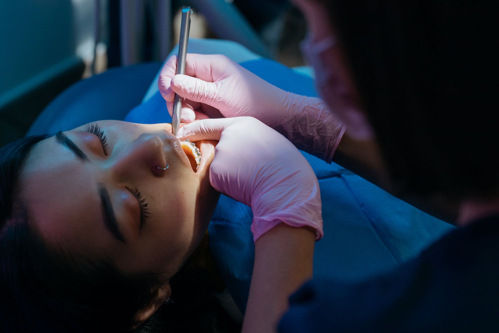 A woman is laying in a dental chair getting her teeth examined by a dentist.