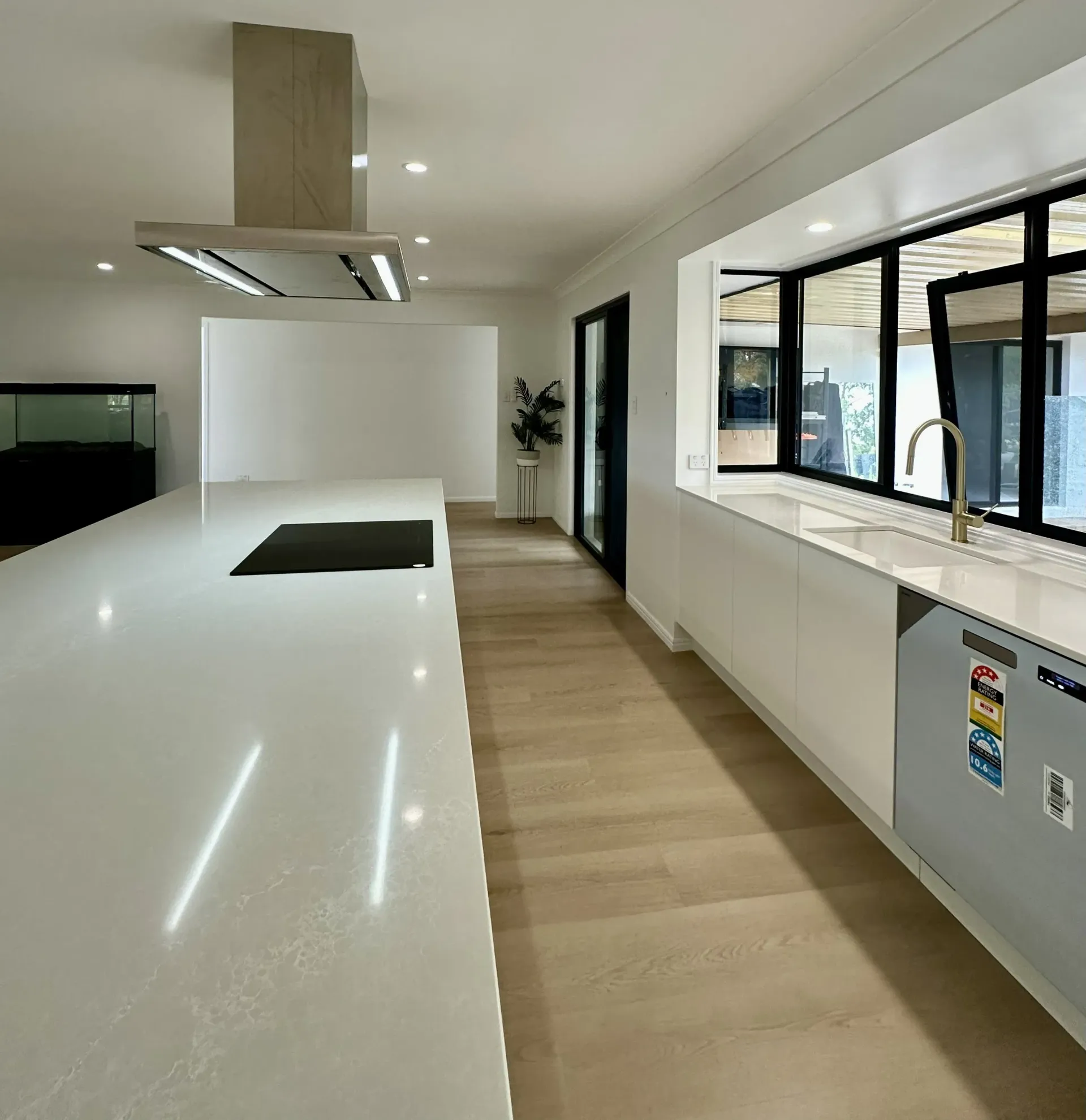 Modern kitchen with white island, stainless steel range hood, light wood floors, and black-framed windows.