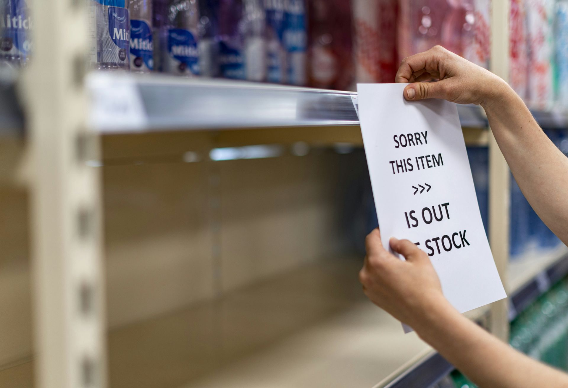 A person is holding a piece of paper in front of an empty shelf in a store.