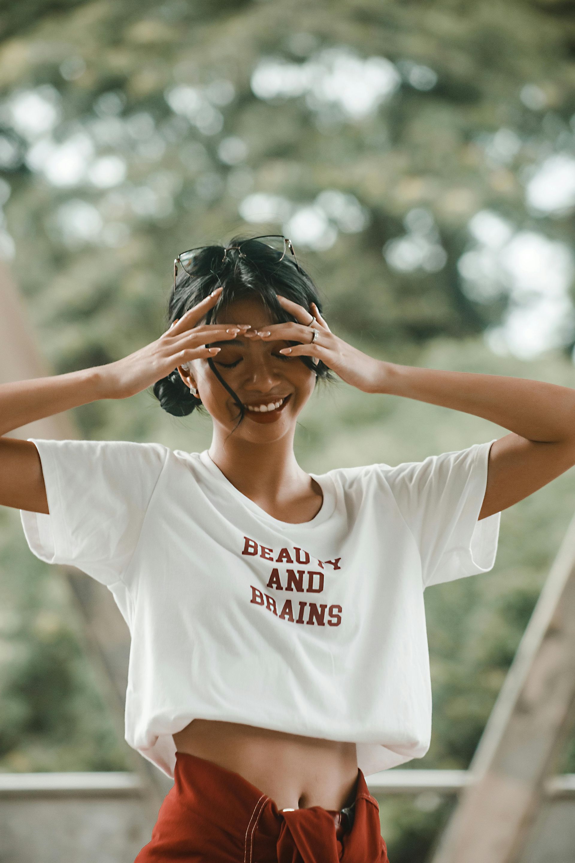 A woman in a white t-shirt is covering her eyes with her hands.